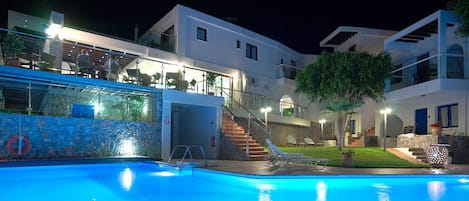 Una piscina con pared de vidrio, una escalera que conduce a un balcón, y un edificio con varios pisos y asientos al aire libre.