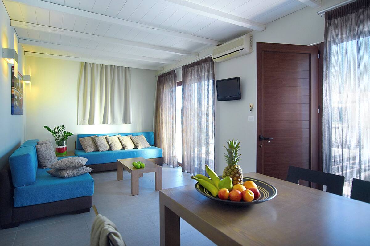 Una sala moderna con un sofá azul, una mesa de centro de madera y una mesa de comedor con un frutero.