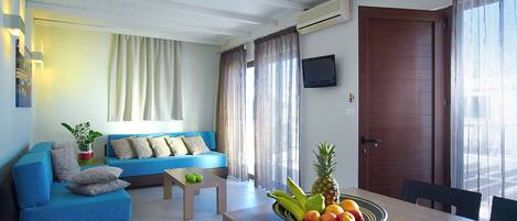 A modern living room with a blue sofa, a wooden table with fruit, and a television on the wall.