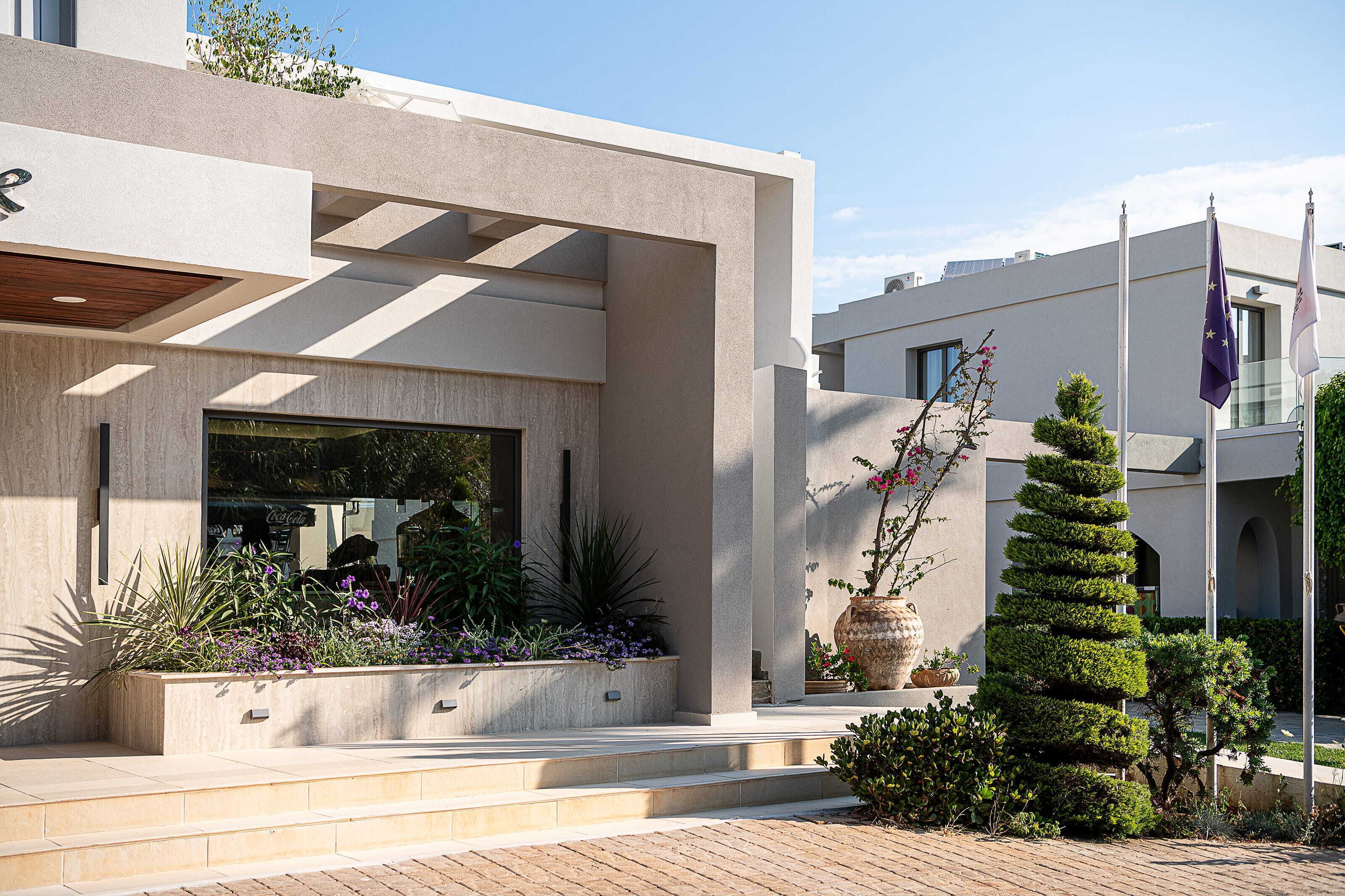A modern building with a concrete facade, a large window, and a well-maintained garden with various plants and flowers.