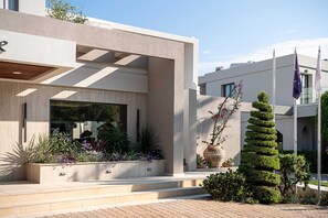 A modern building with a concrete facade, a large window, and a well-maintained garden with various plants and flowers. - Minos Village (Chania)