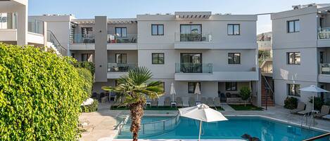 A modern apartment building with a swimming pool, outdoor seating, and a well-maintained garden.