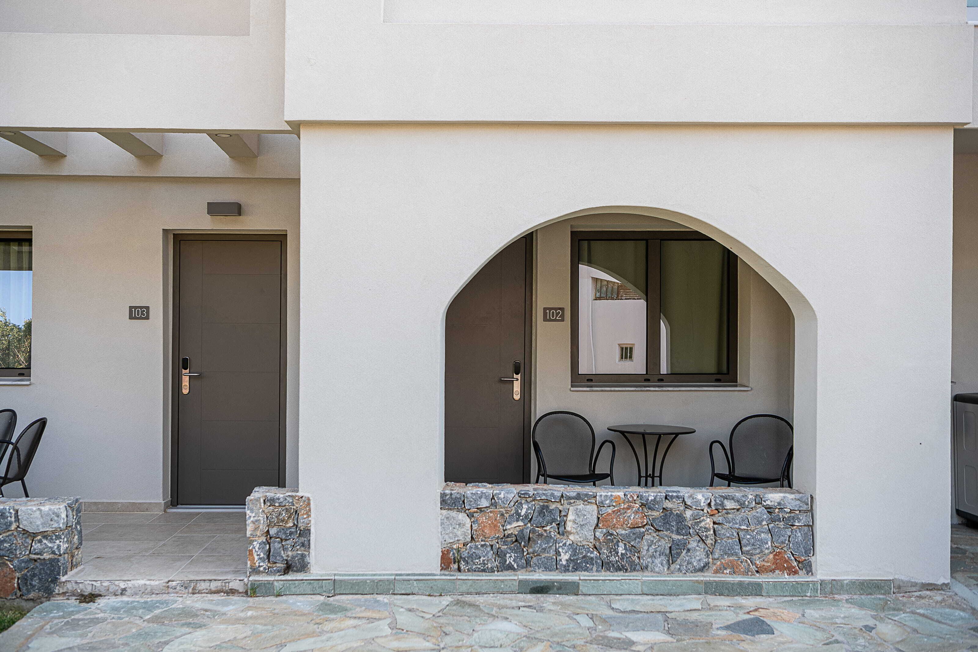 A building entrance with a stone wall, two chairs, and a door marked with the number 103.