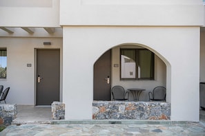 Entrada de um edifício com um muro de pedra, duas cadeiras e uma porta com o número 103.
