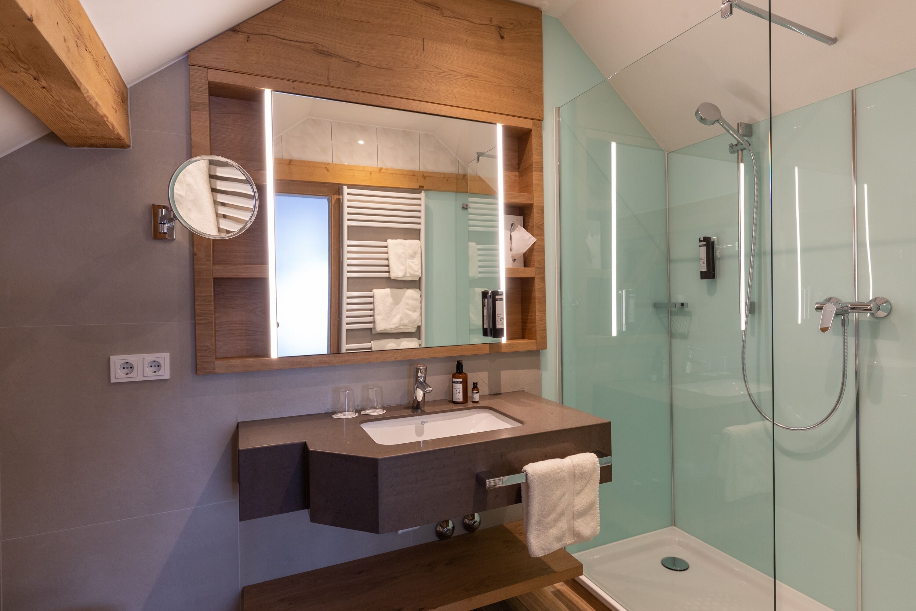 Ein modernes Badezimmer mit einem Holzkonsolenunterschrank, einem großen Spiegel, einer Glasdusche und einem festen Handtuchhalter.