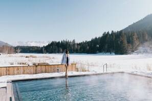 Una persona de pie junto a una piscina, con un paisaje nevado y montañas al fondo.
