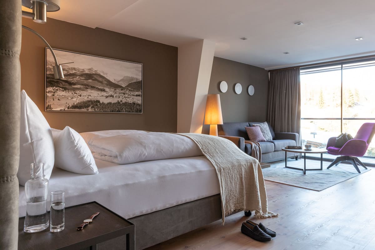 Ein modernes Hotelzimmer mit einem großen Bett, einer Couch, einem Couchtisch und Blick ins Freie.