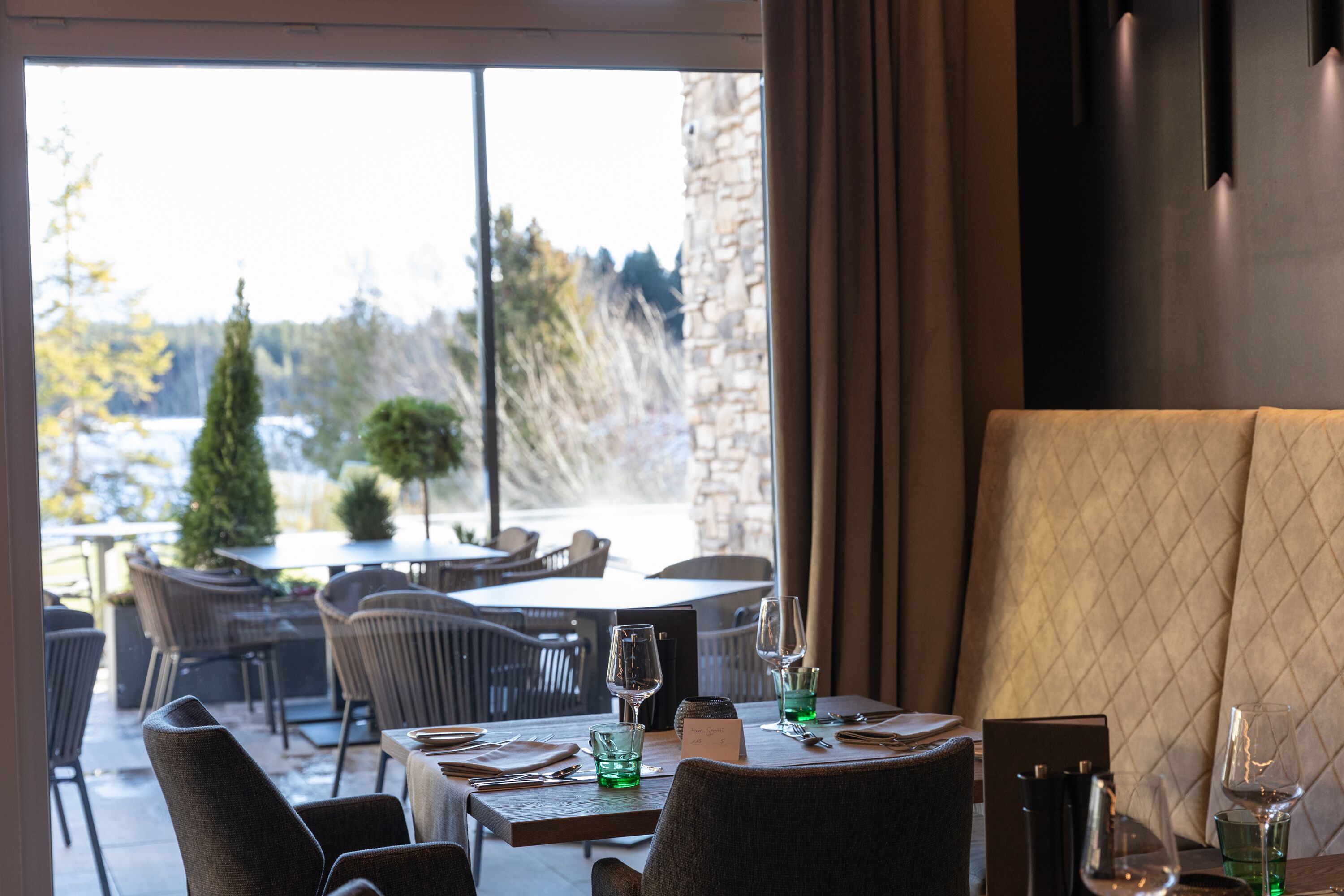 Un restaurante con terraza, paredes de piedra y vistas a árboles y un edificio.