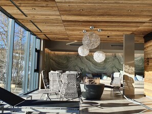 A modern interior with a wooden ceiling, large windows, and a seating area with wicker chairs and a black ottoman. - Hotel Seespitz Seefeld Superior - Adults & Residents Only (Seefeld in Tirol)