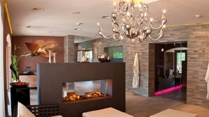 Een moderne lobby met een open haard, een kroonluchter en uitzicht op een wellnessruimte.