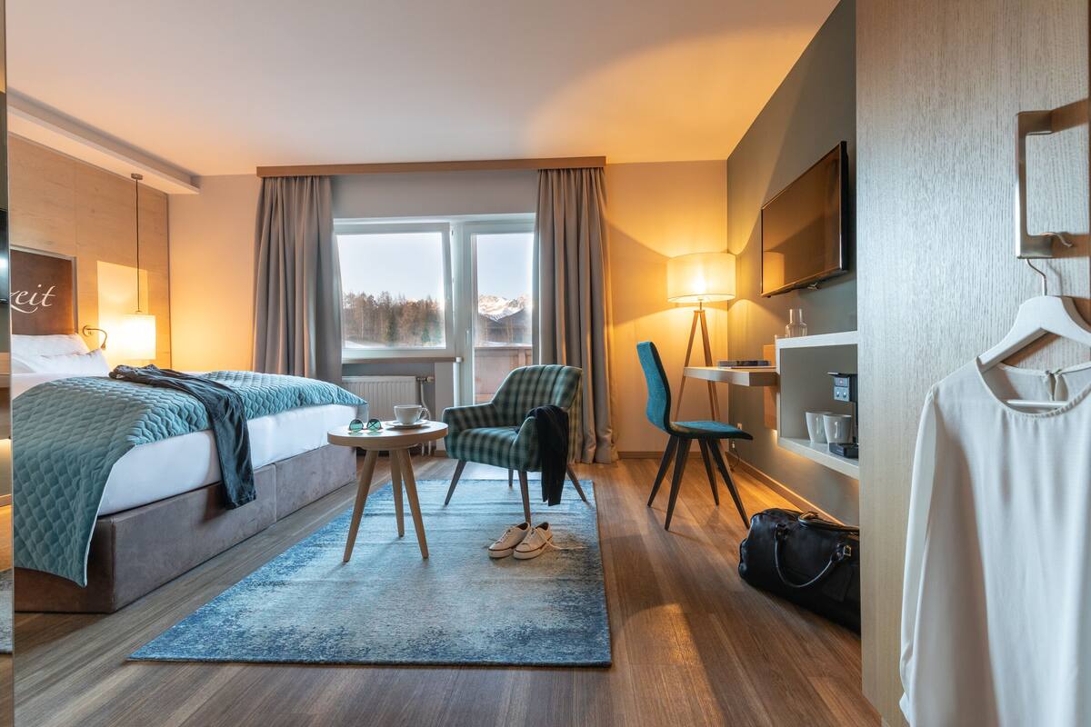Ein Hotelzimmer mit Bett, Sessel, Tisch, Fernseher und einem Fenster mit Bergblick.