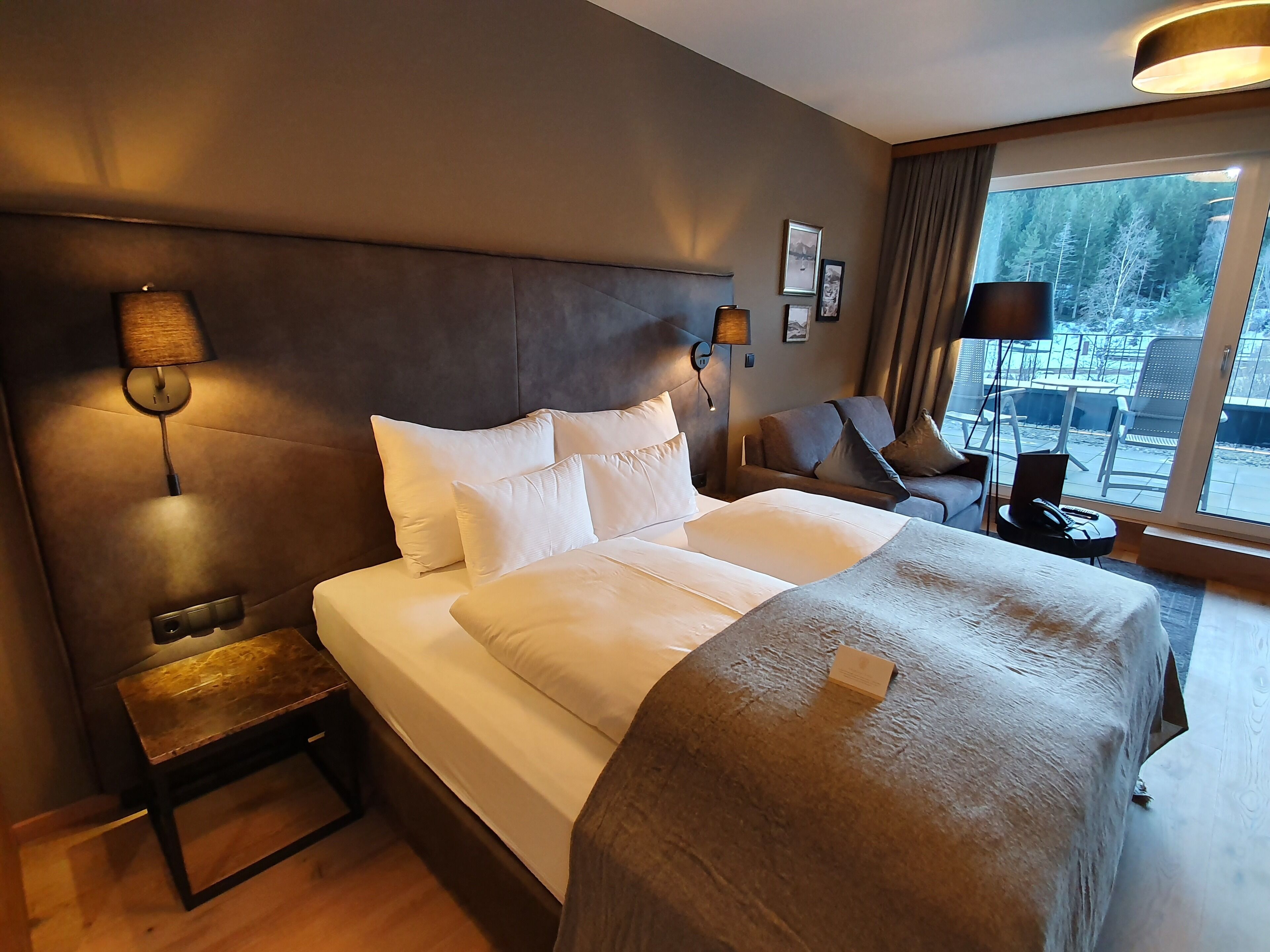 Habitación de hotel con una cama grande, una mesita de noche, una lámpara, una silla y vistas al exterior.