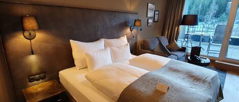 Habitación de hotel con una cama grande, una mesita de noche, una lámpara, una silla y vistas al exterior.
