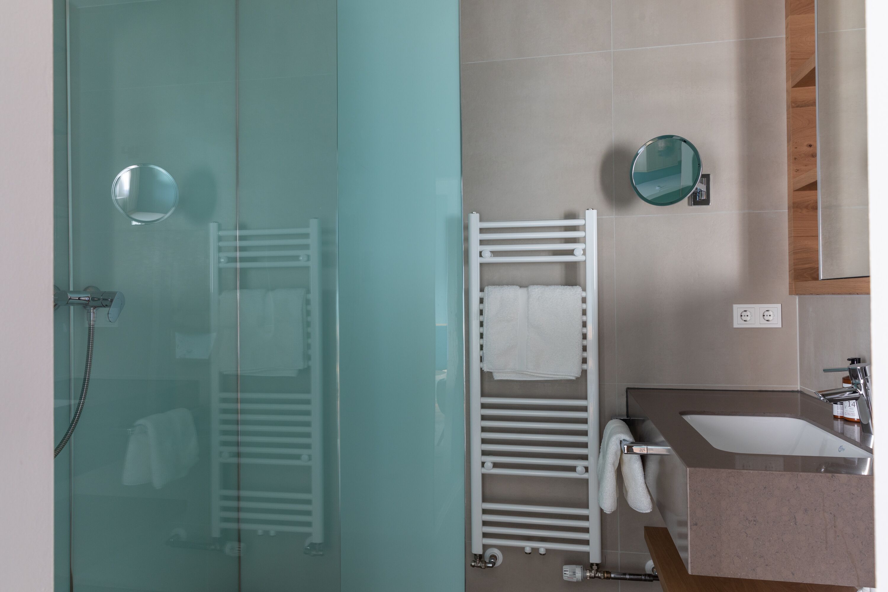 Un baño moderno con cabina de ducha de vidrio, un perchero blanco, un lavamanos con espejo y una pared de acento de madera.
