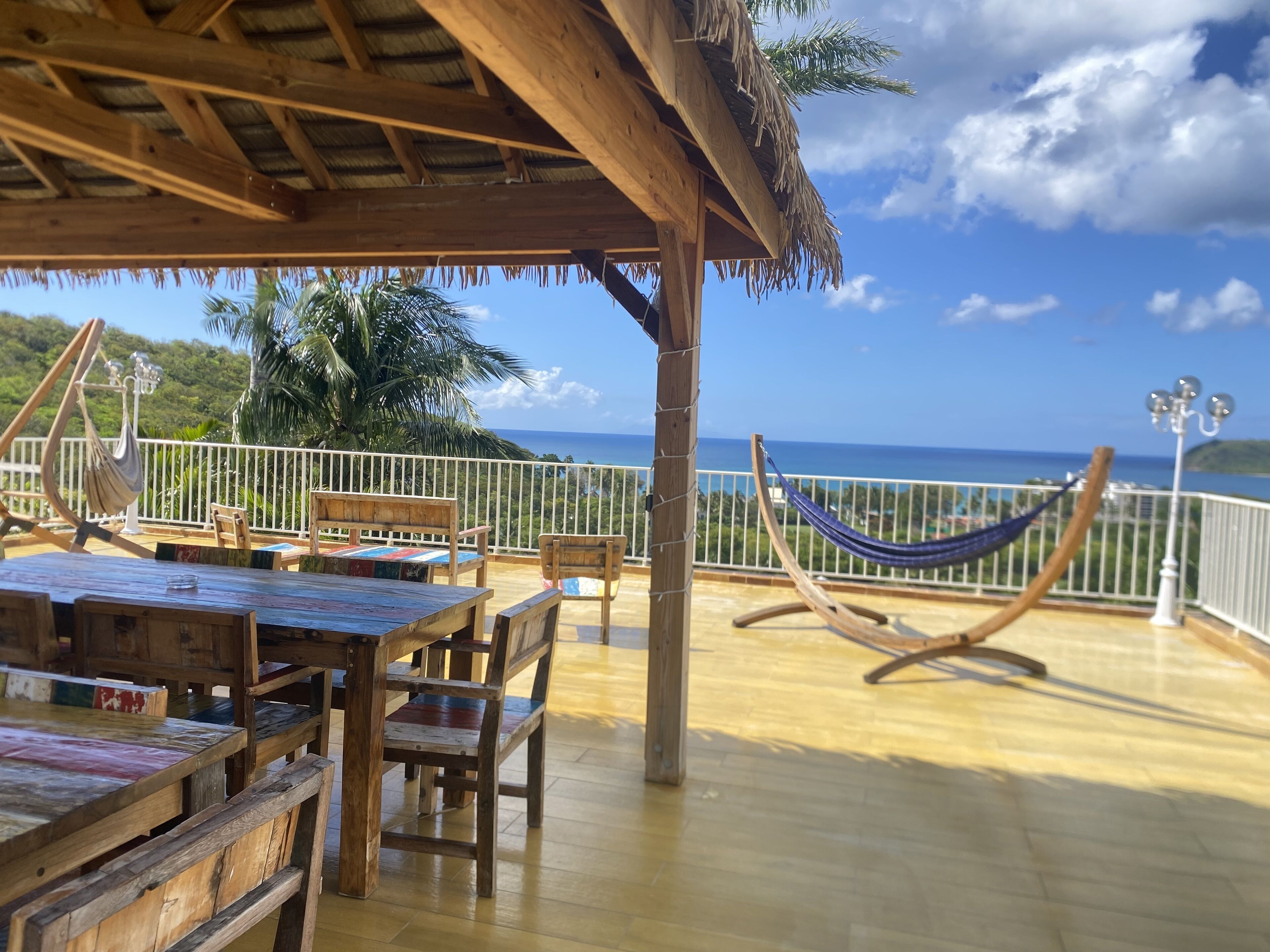 Una terraza de madera con techo de paja, muebles de madera y una hamaca.