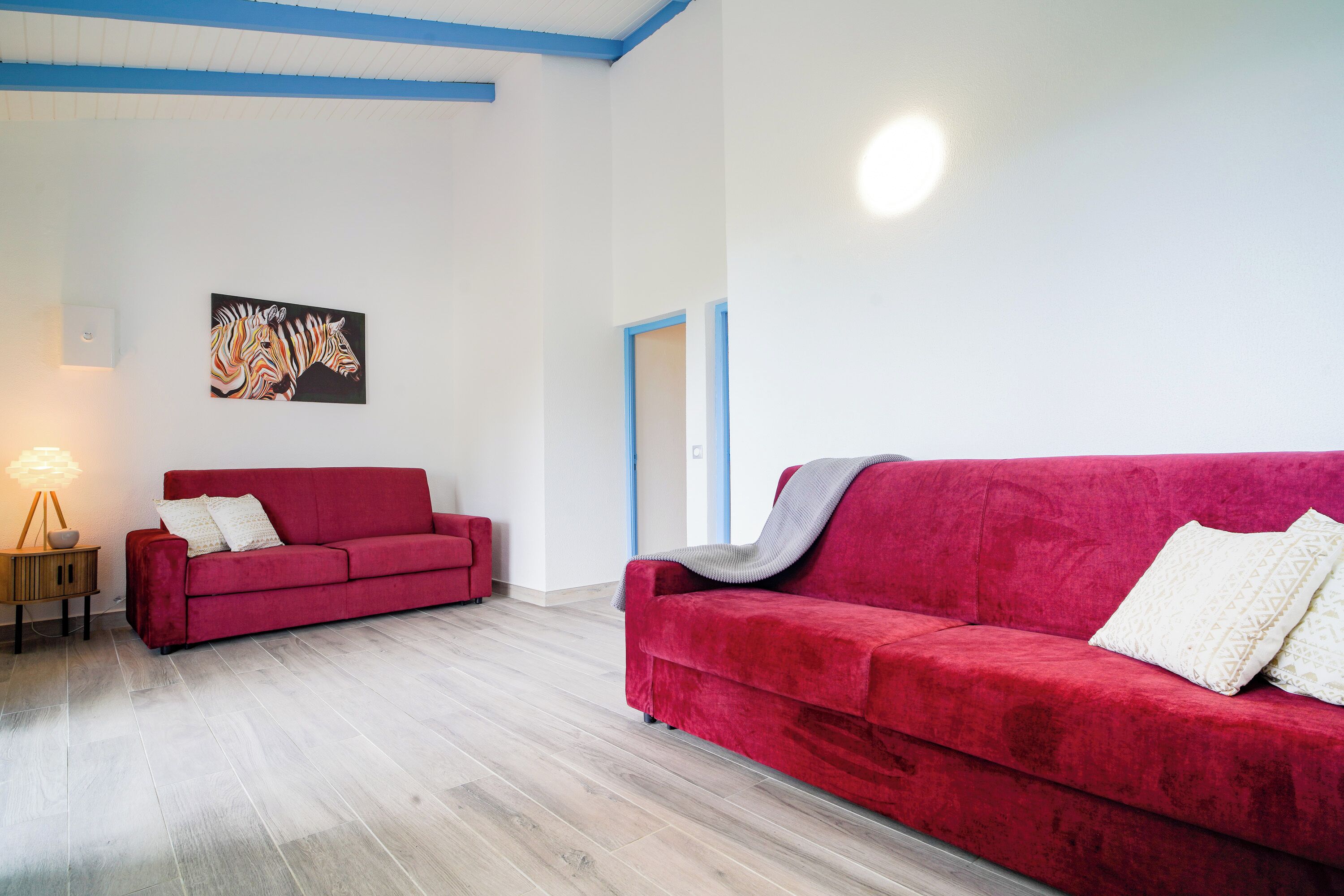 A room with two red sofas, a wooden floor, and a zebra painting on the wall.