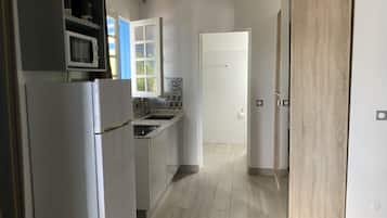 Eine Küche mit Kühlschrank, Mikrowelle, Spüle und Schränken. Eine Tür führt in einen anderen Raum.