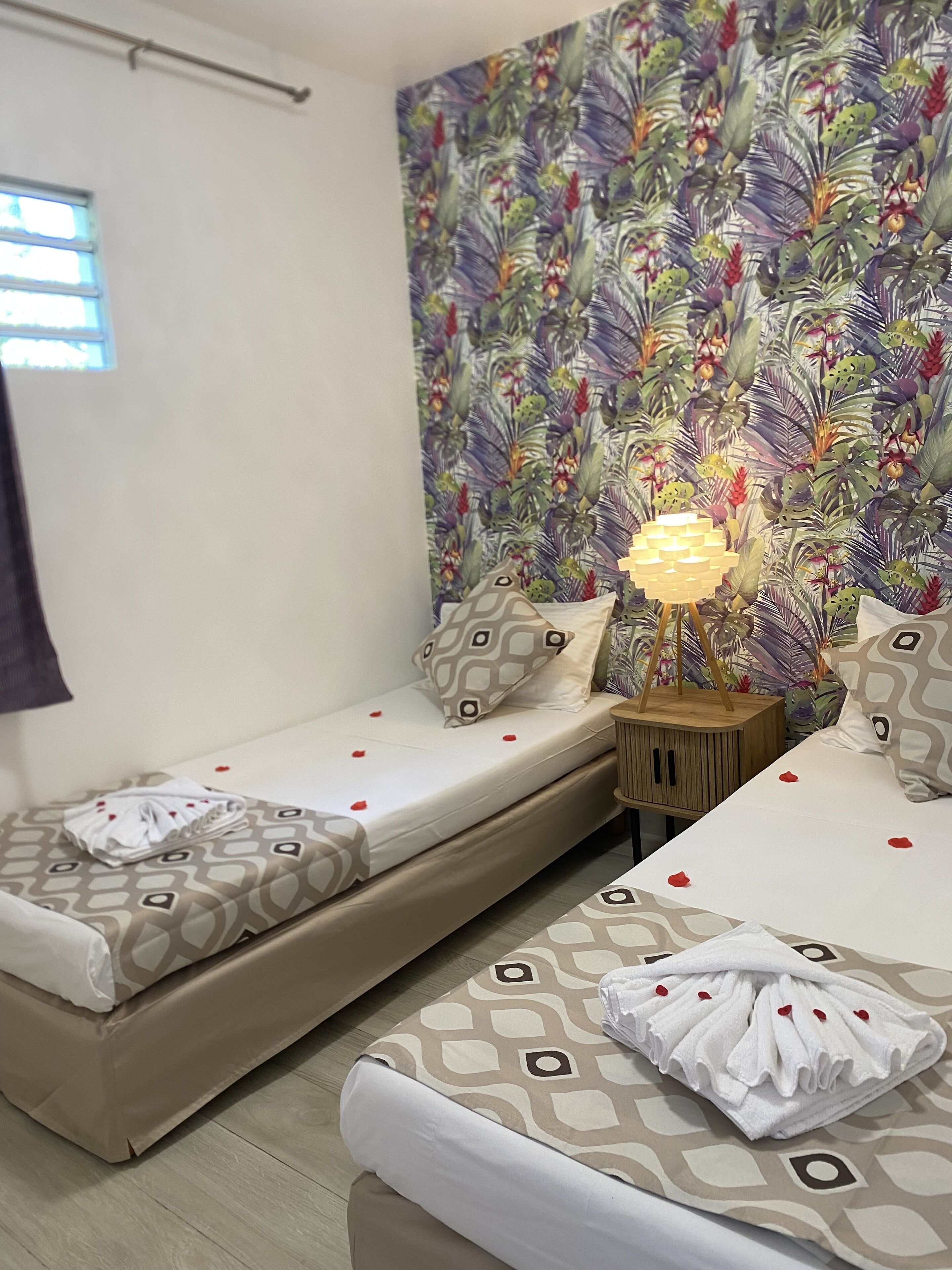 Une chambre d’hôtel avec deux lits simples, un mur décoré de motifs, une lampe de chevet et une fenêtre.