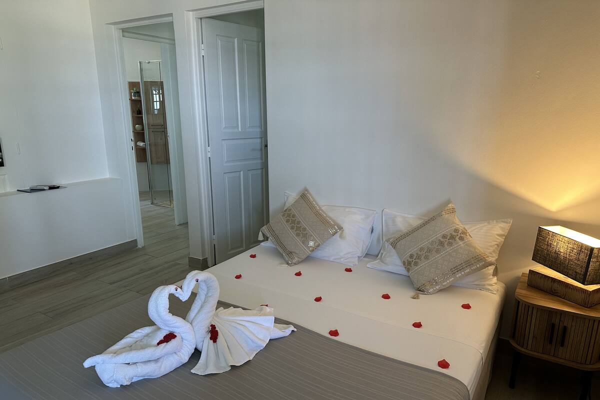 Une chambre d’hôtel avec un lit, deux oreillers, une table de chevet avec une lampe et une sculpture réalisée avec des serviettes, placée sur le lit.