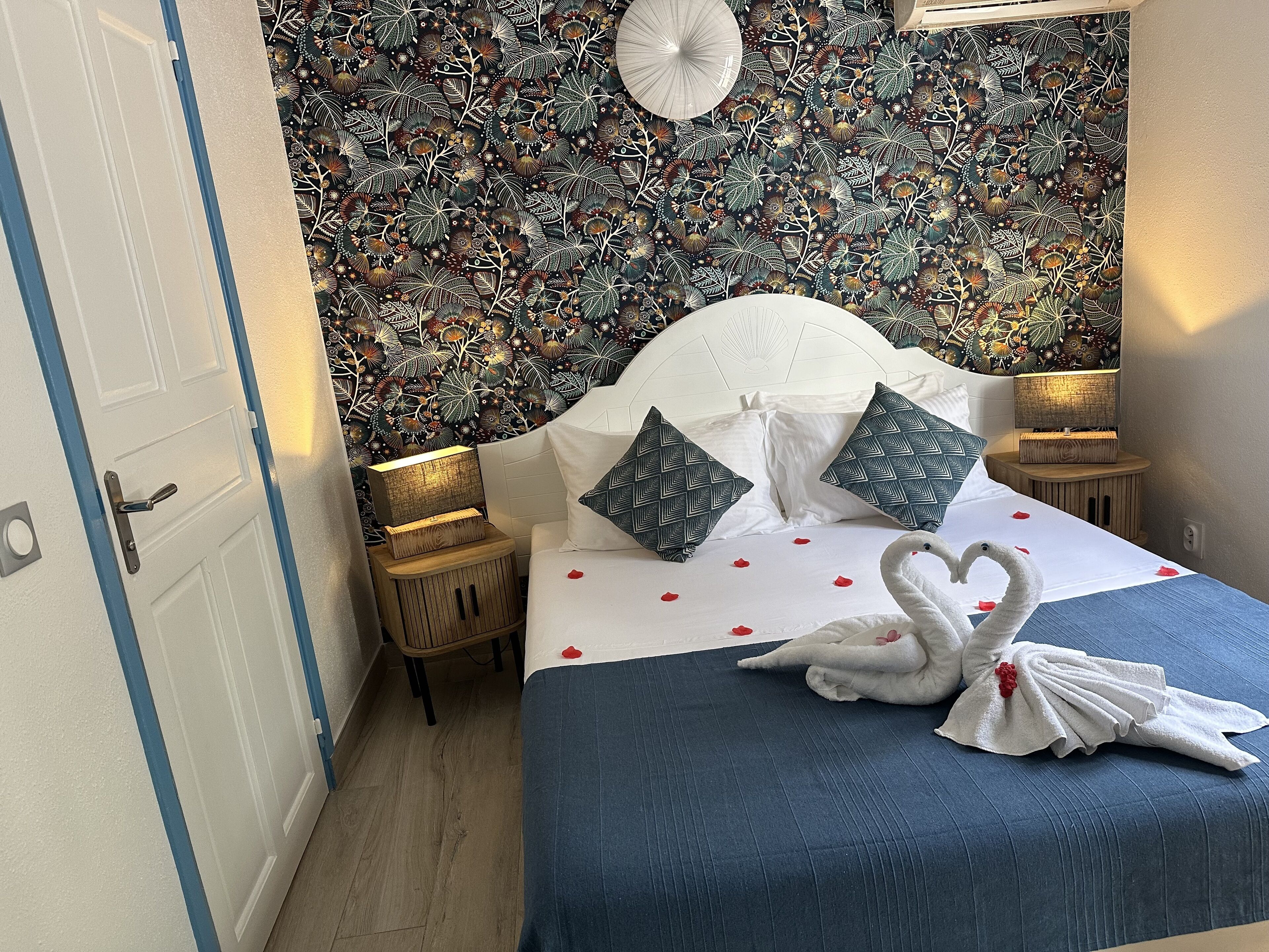 A neatly made bed with a blue bedspread, white pillows, and a decorative swan towel.