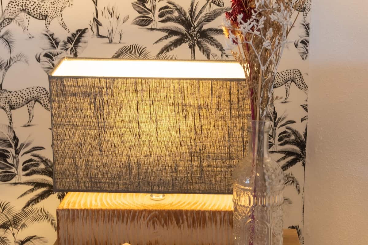 Une table de chevet en bois sur laquelle se trouve un livre intitulé « Nicholls In Jour » et un vase contenant des fleurs séchées.