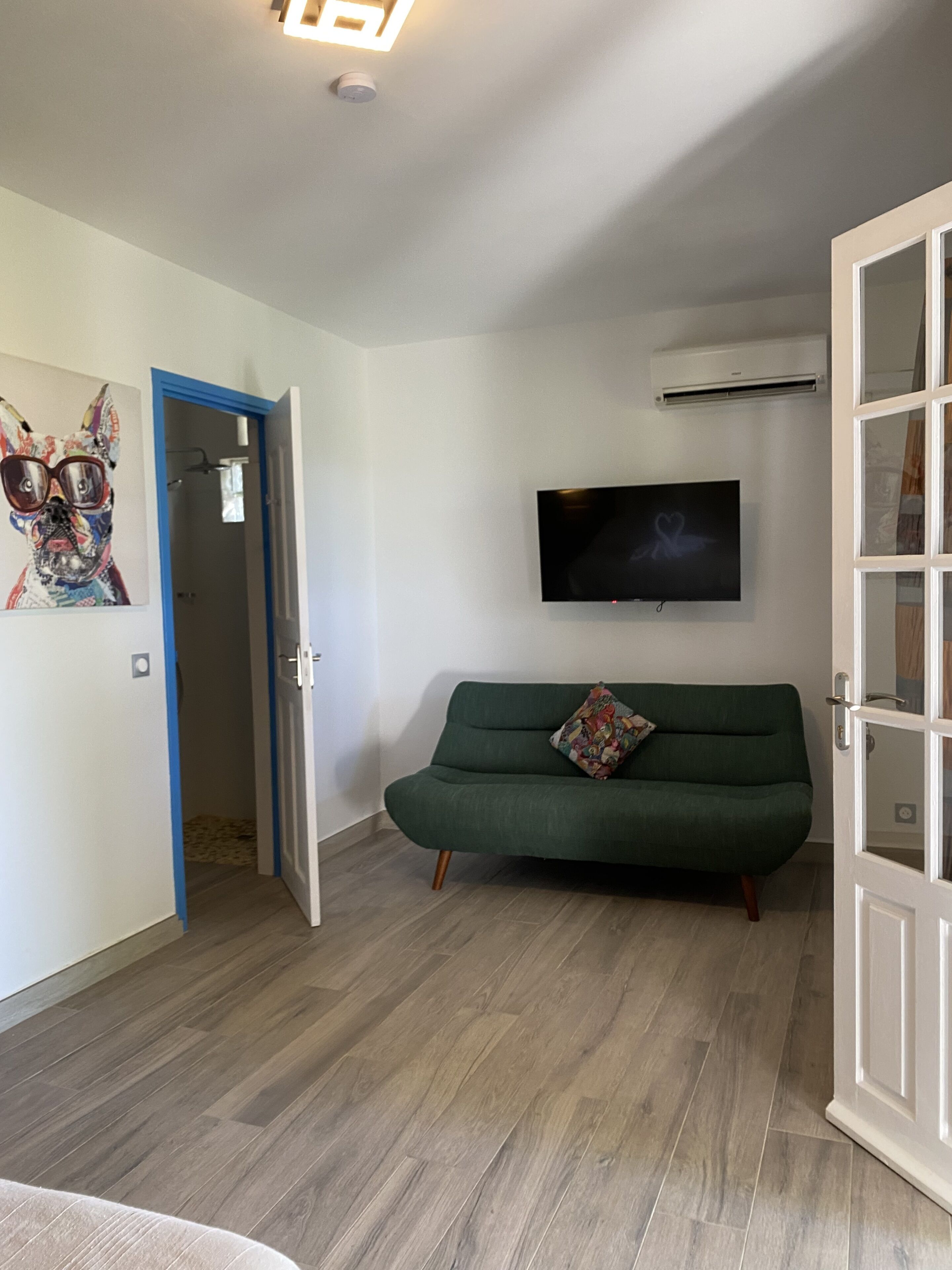 A room with a green sofa, a flat-screen TV mounted on the wall, and a wooden floor.