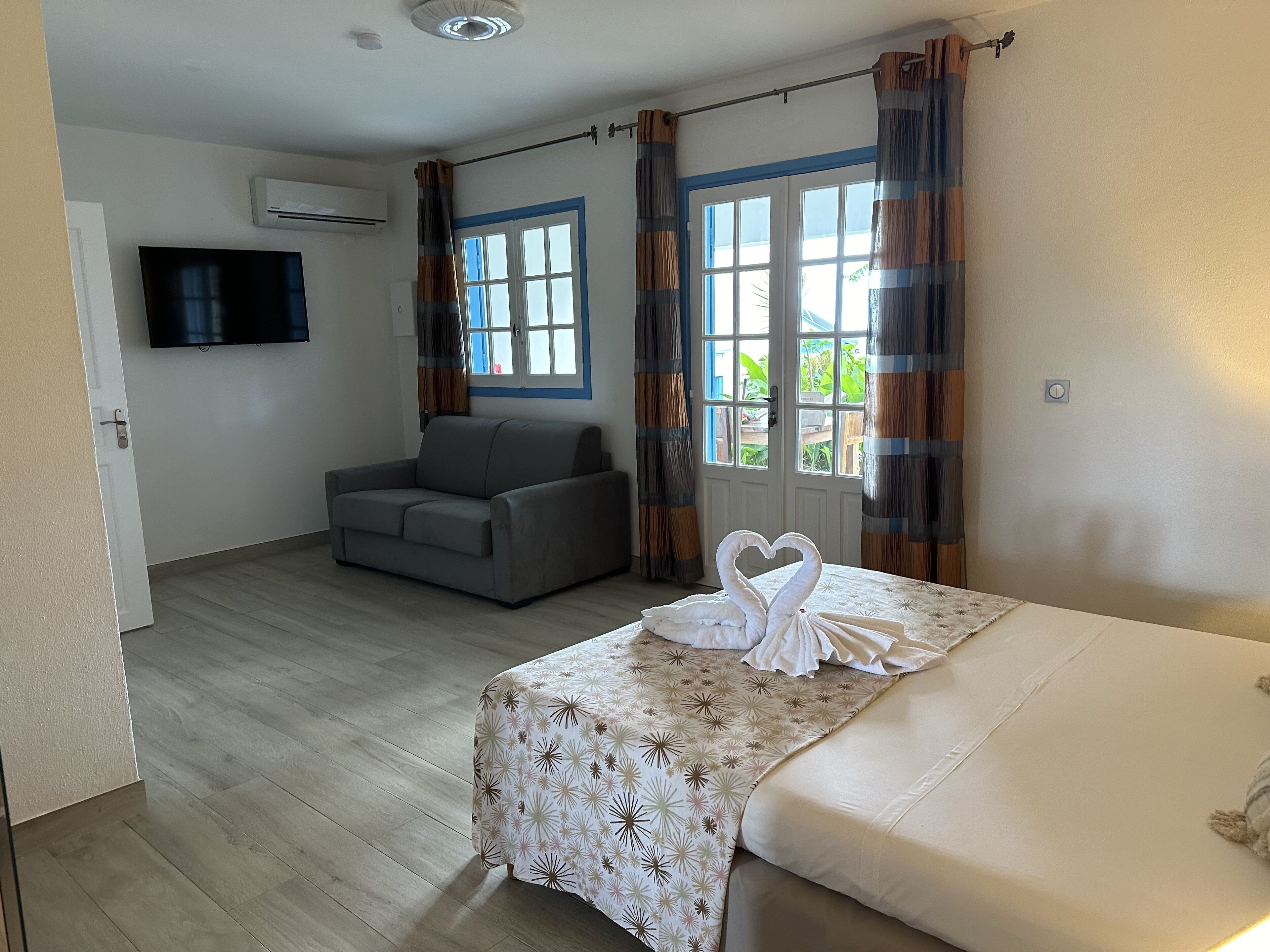 Quarto com cama, sofá, televisão e janela com cortinas.