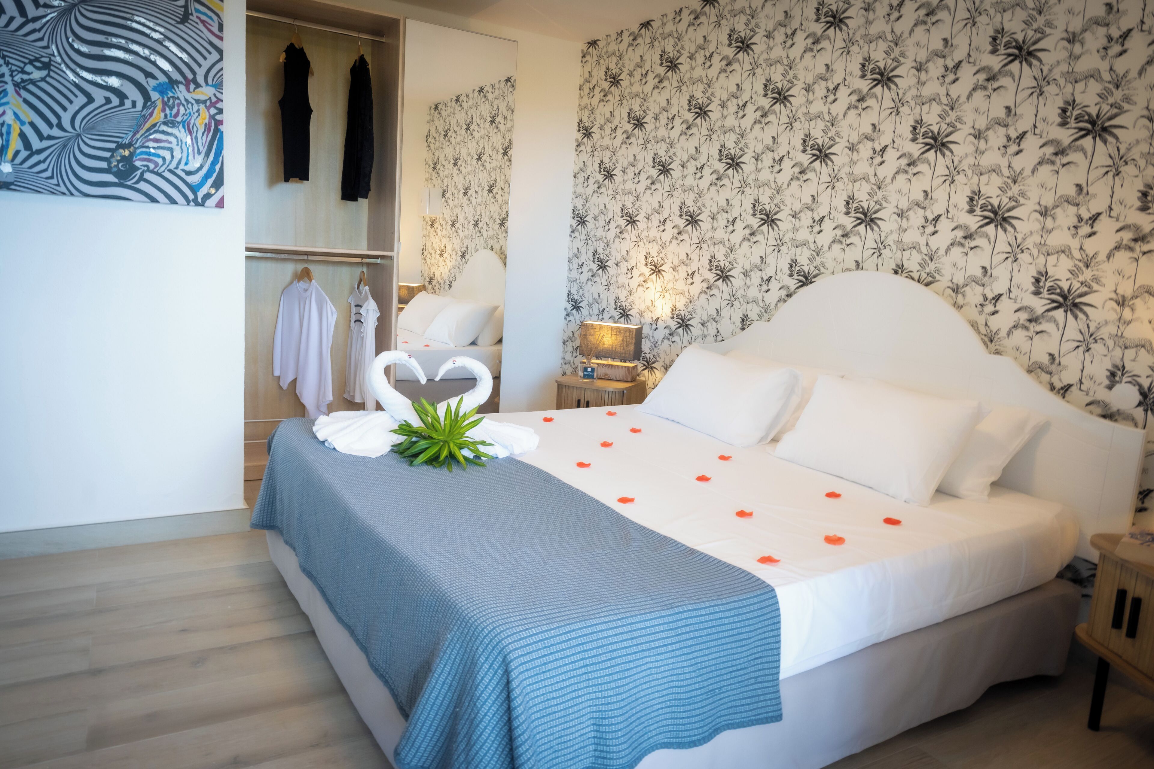 A neatly arranged bedroom with a large bed, a wardrobe, and a mirror.