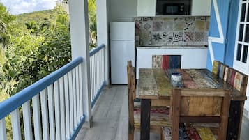 A covered outdoor dining area with a wooden table and chairs, a white refrigerator, and a microwave above a tiled backsplash.