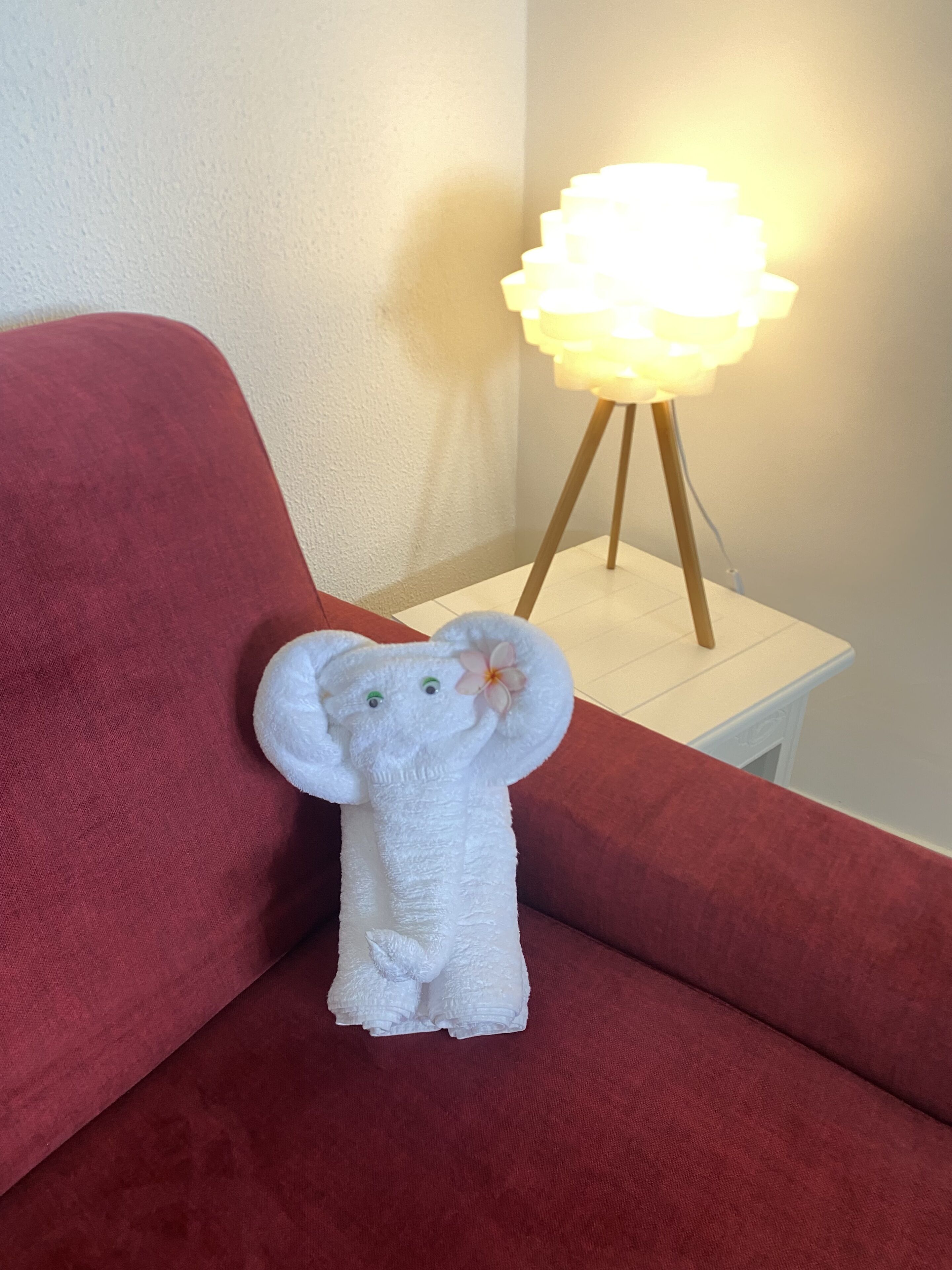 A plush elephant toy on a red couch with a white lamp on a white side table beside it.