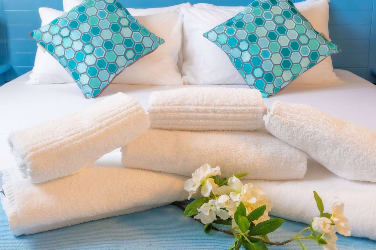 Un lit bien fait, avec du linge de lit blanc et deux coussins à motifs, une tête de lit bleue et un papier peint à fleurs en arrière-plan.