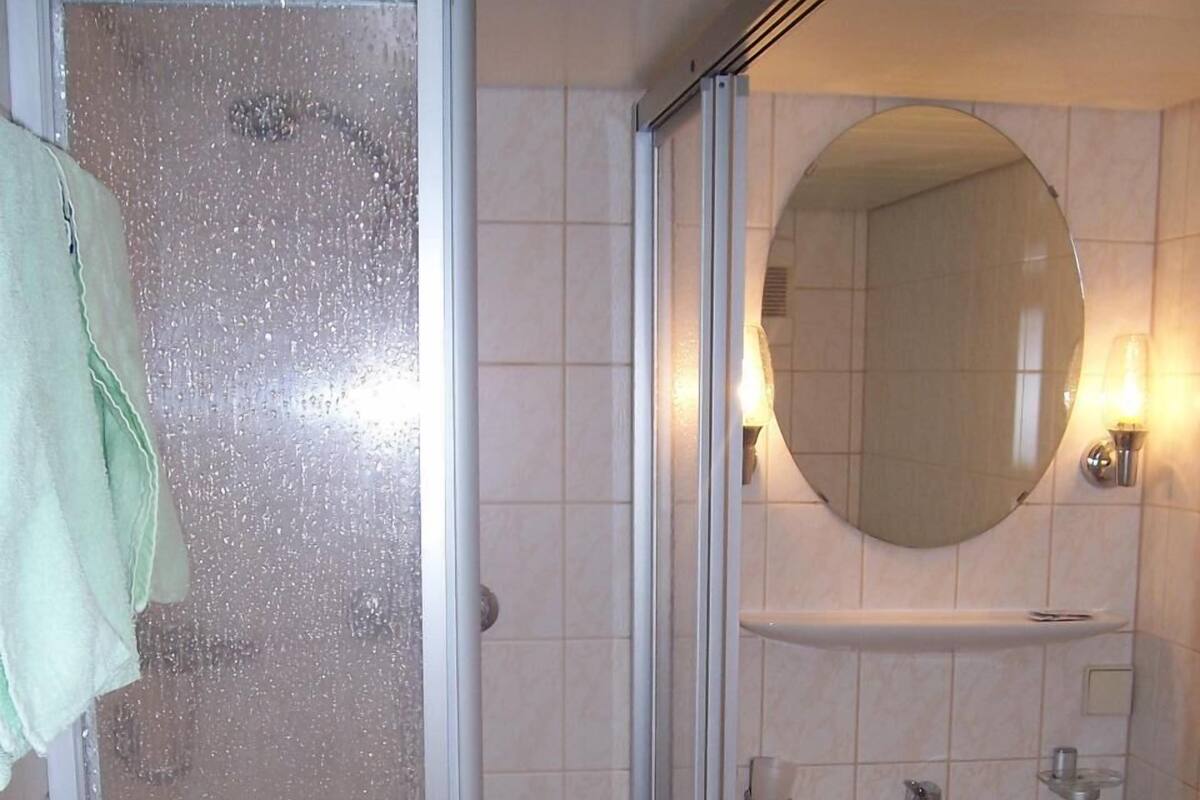 A bathroom with a glass shower enclosure, a sink, and a mirror.
