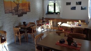 A dining area with wooden tables and chairs, a stone wall, and a window with curtains. - Gasthof Thomas-Müntzer (Neuhaus am Rennweg)
