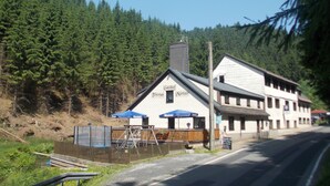A building with a white facade and a dark roof, surrounded by dense forest. - Gasthof Thomas-Müntzer (Neuhaus am Rennweg)