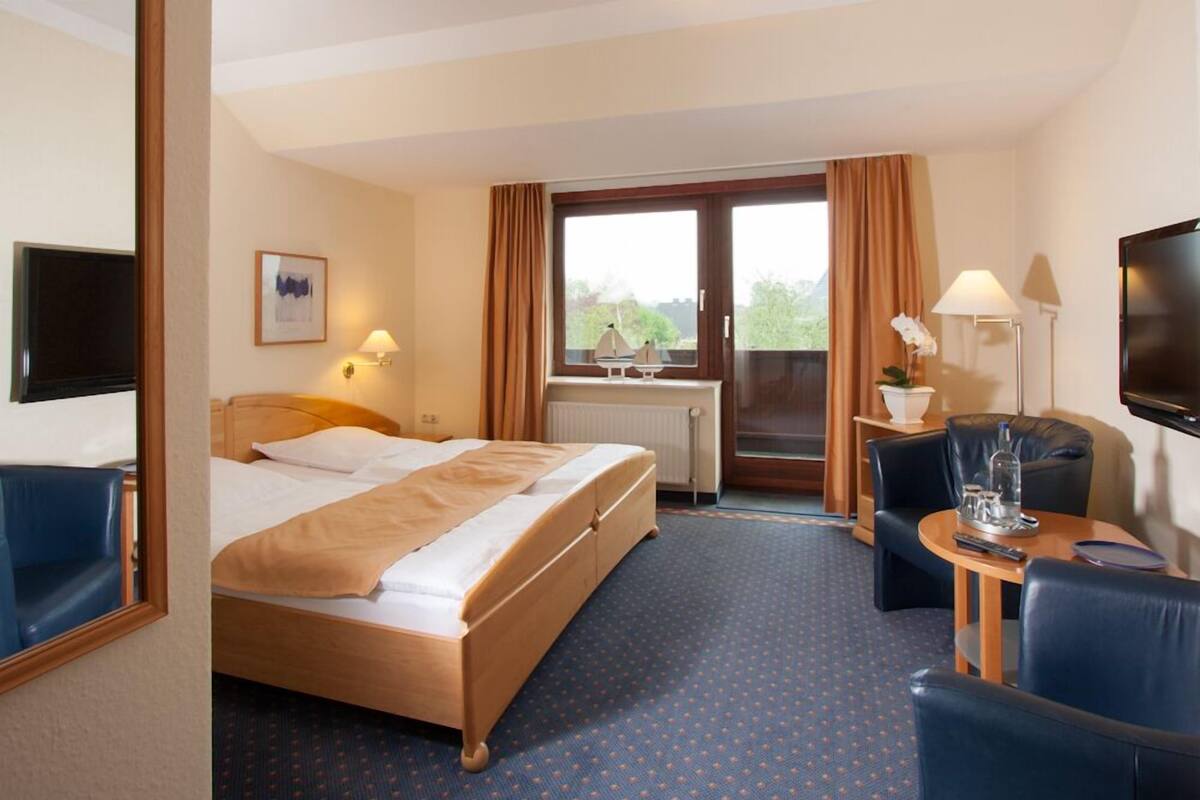 A hotel room with a bed, a desk with a chair, a TV, and a window with curtains.