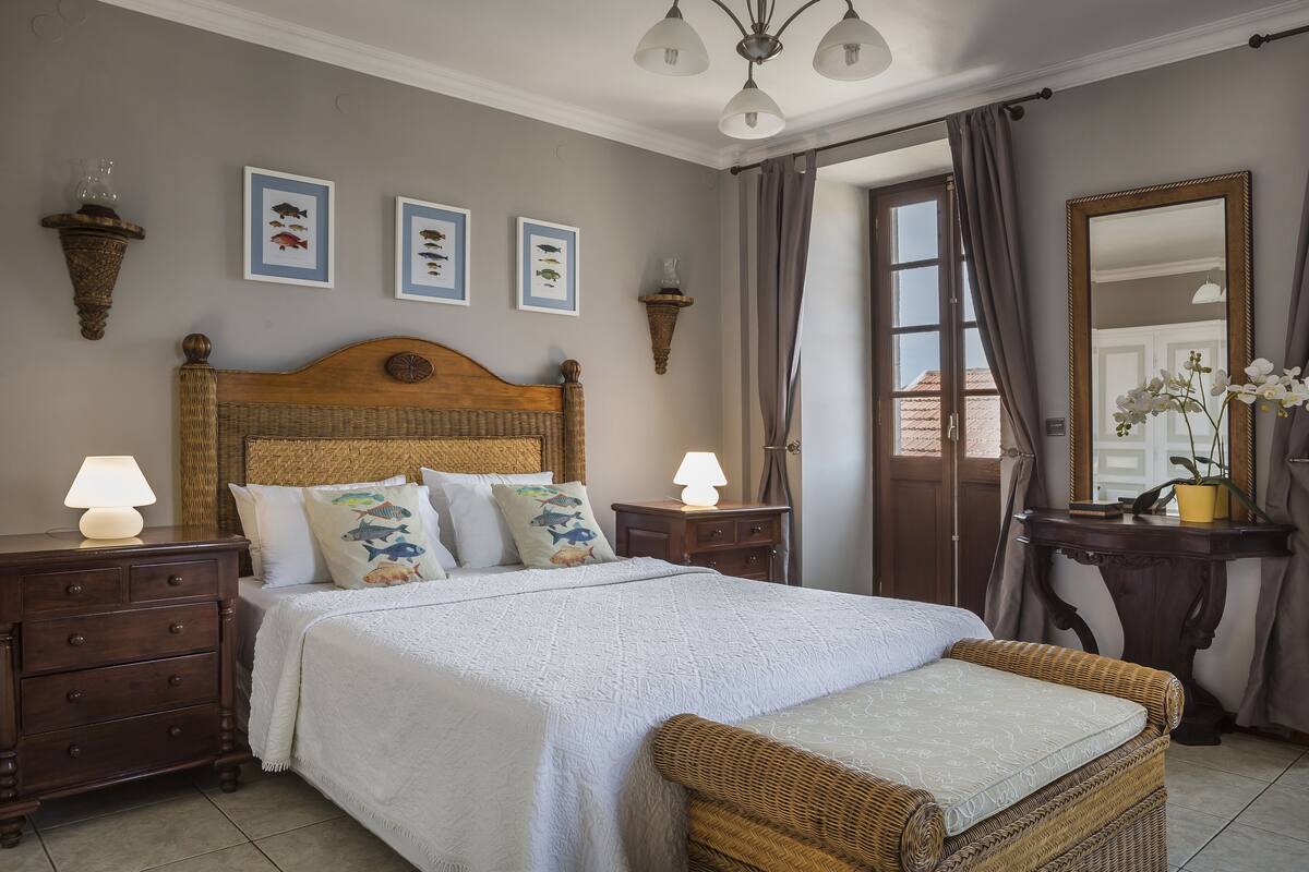 A bedroom with a wooden headboard, a bed with white bedding, two bedside tables with lamps, and wall-mounted fish-themed artwork.