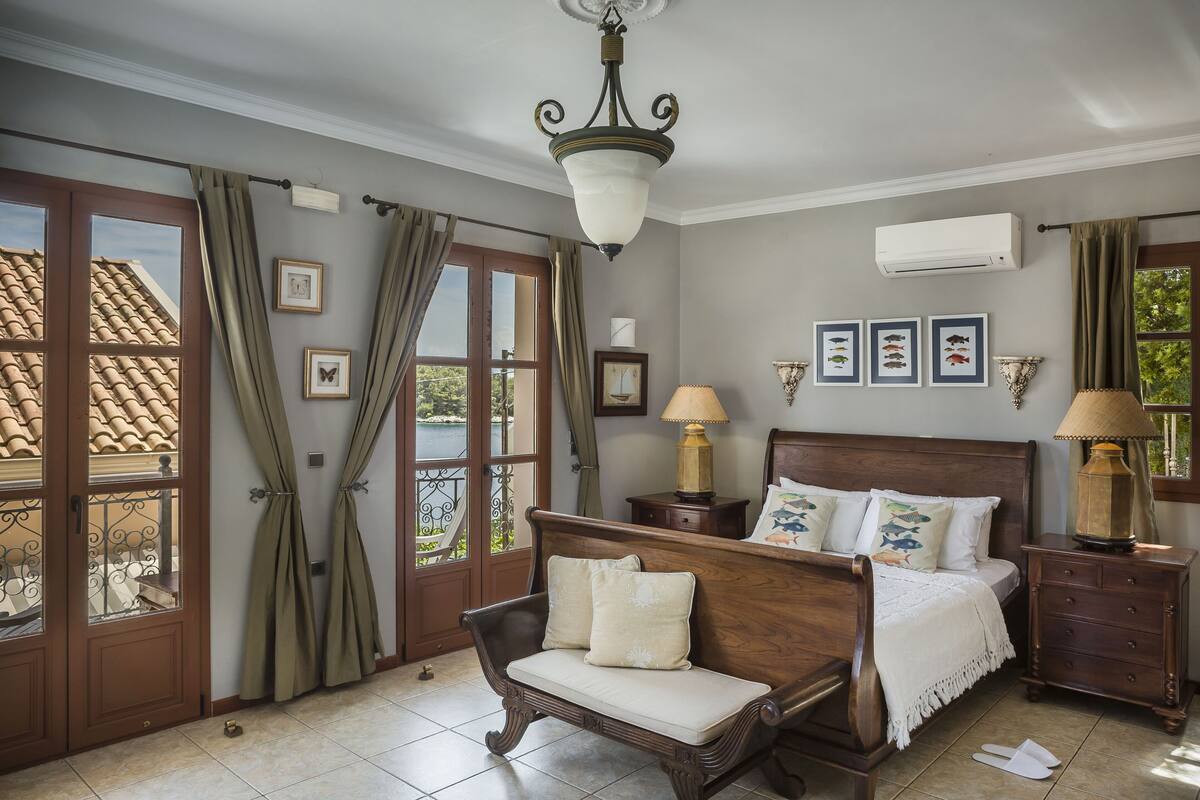 A bedroom with a wooden bed, two bedside tables, a chandelier, and a view of the outside.