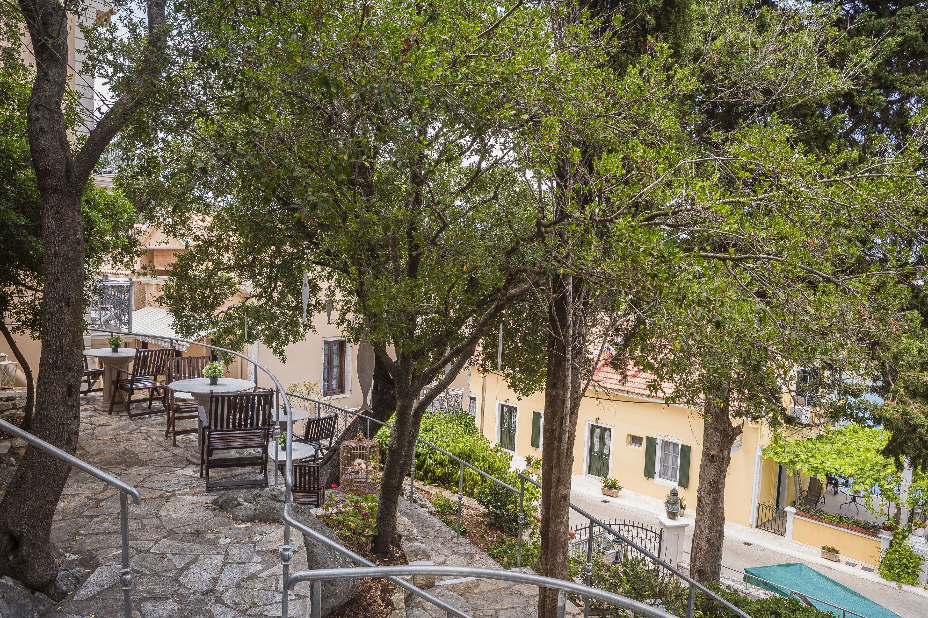 A stone staircase leading to outdoor seating with tables and chairs, surrounded by trees and buildings.