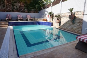 A swimming pool with blue tiles, a brick wall, and potted plants. - Faros Suites - Adults Only (Kefalonia)