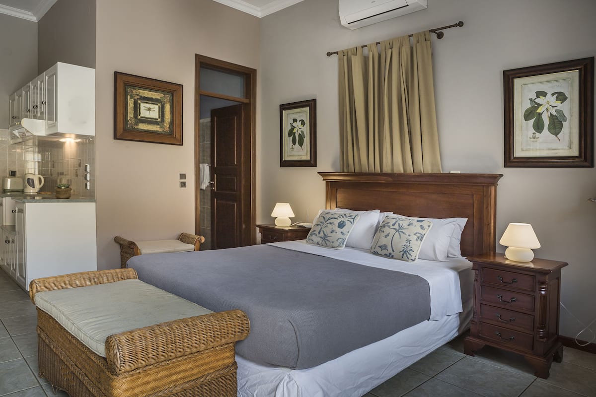 A neatly arranged bedroom with a bed, bedside tables, a chair, and a small kitchenette.