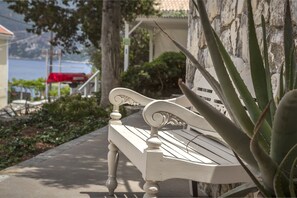 A white bench with ornate carvings, positioned on a paved path beside a stone wall with aloe plants. - Faros Suites - Adults Only (Kefalonia)