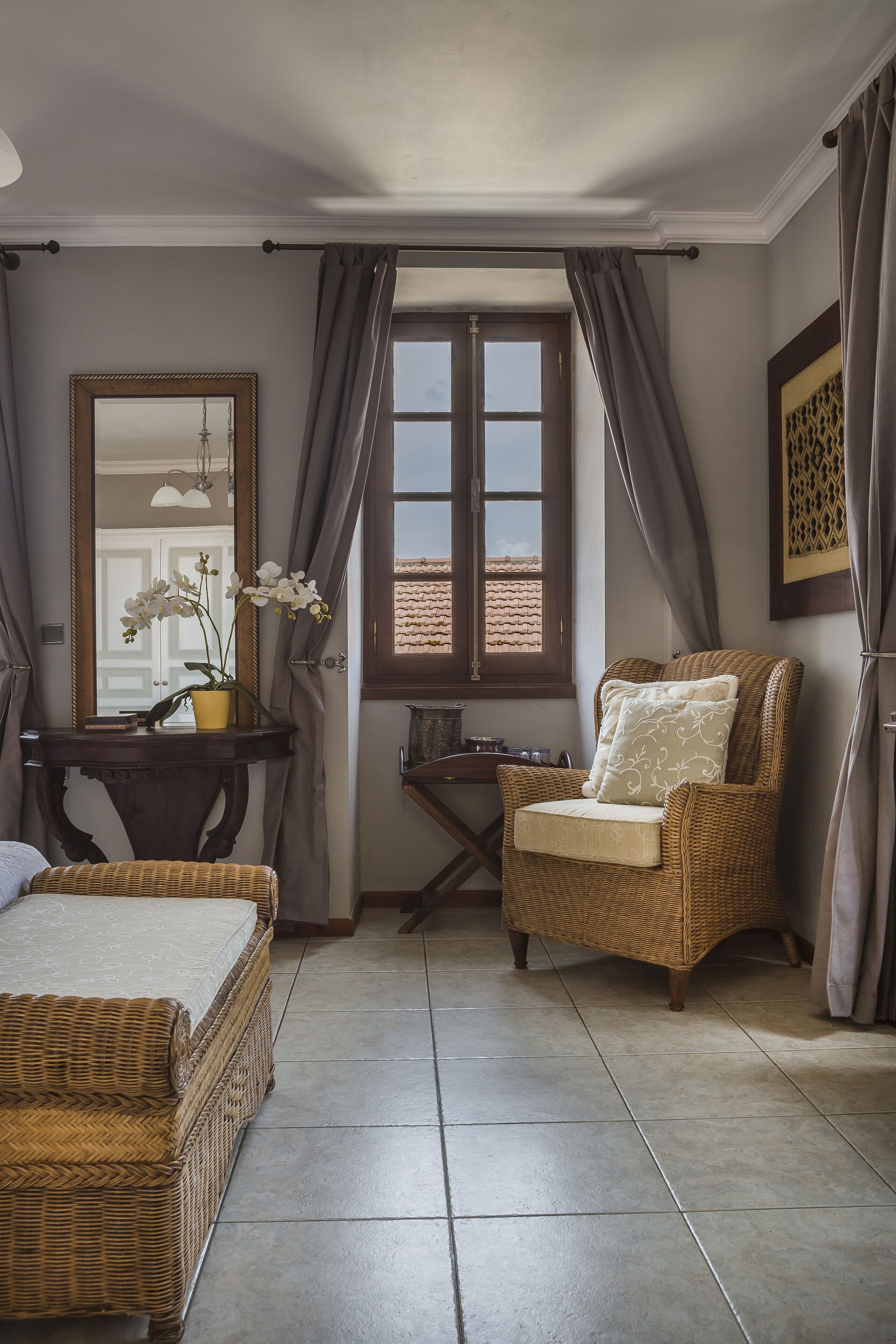 A room with a wicker sofa, a chair, a table with a mirror, and a potted orchid.