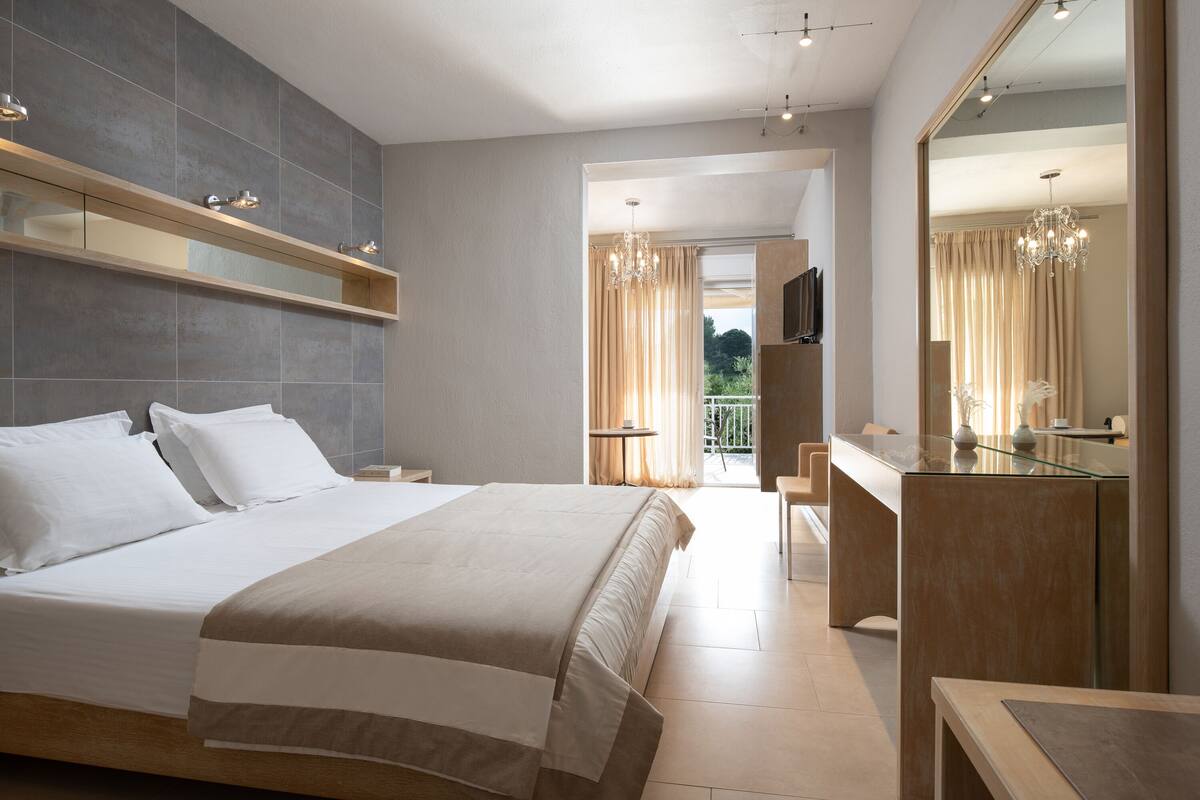 Una habitación de hotel moderna con una cama grande, un tocador con cristal y un balcón con cortinas.