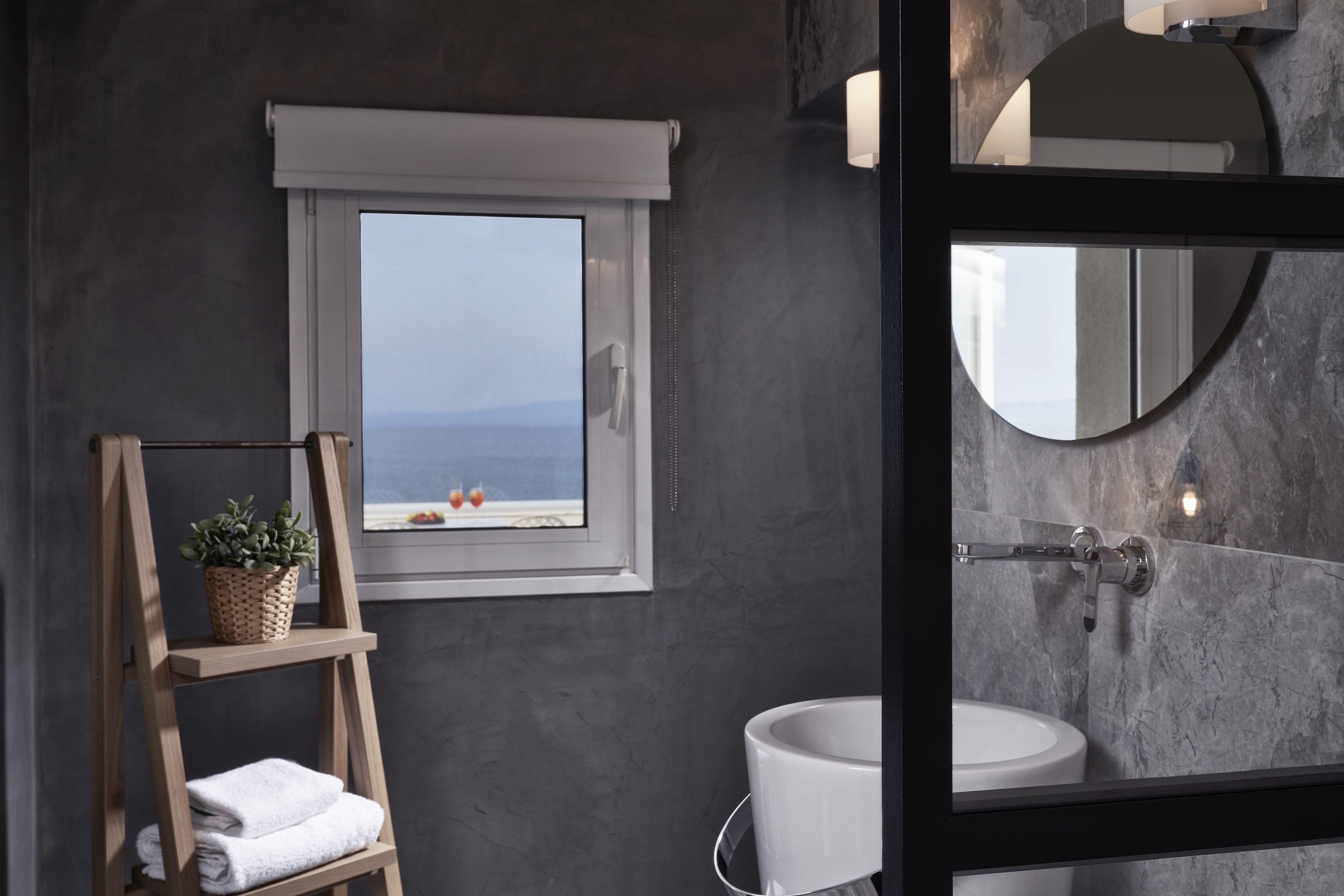 Un baño con ventana, repisa de madera con toallas, lavamanos y espejo.