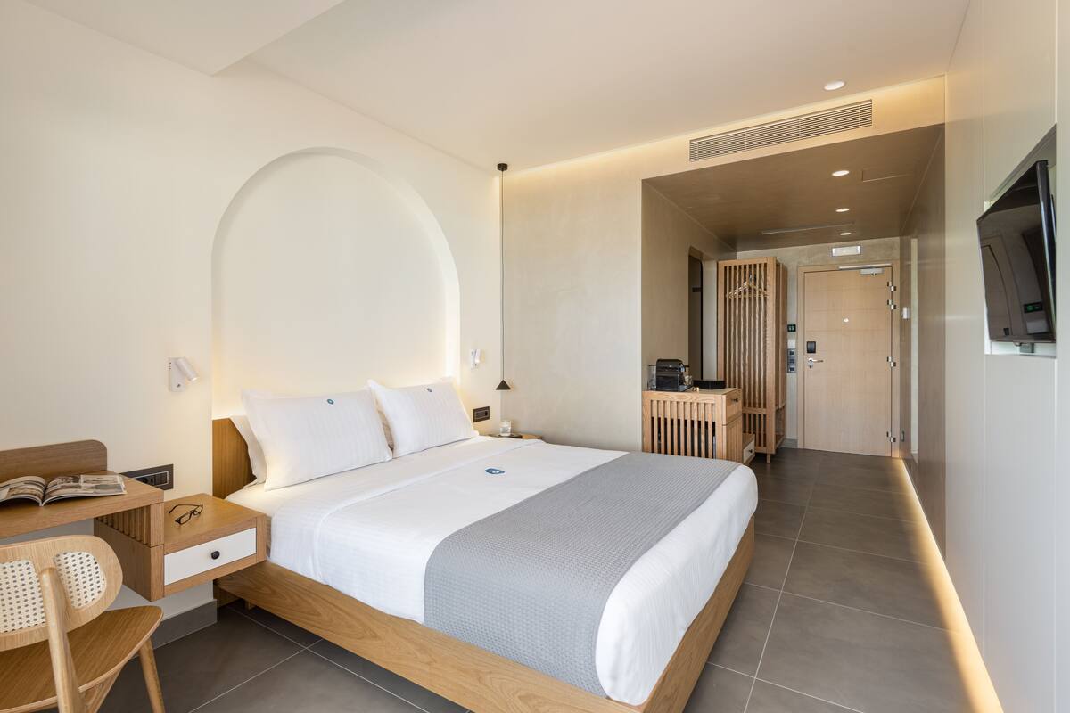 Una habitación de hotel moderna con una cama grande, un escritorio con silla, un televisor y un baño visible a través de una puerta abierta.