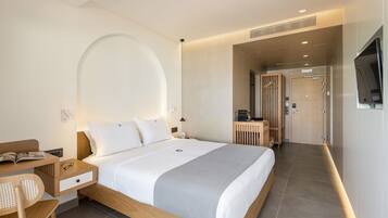 Una habitación de hotel moderna con una cama grande, un escritorio con silla, un televisor y un baño visible a través de una puerta abierta.