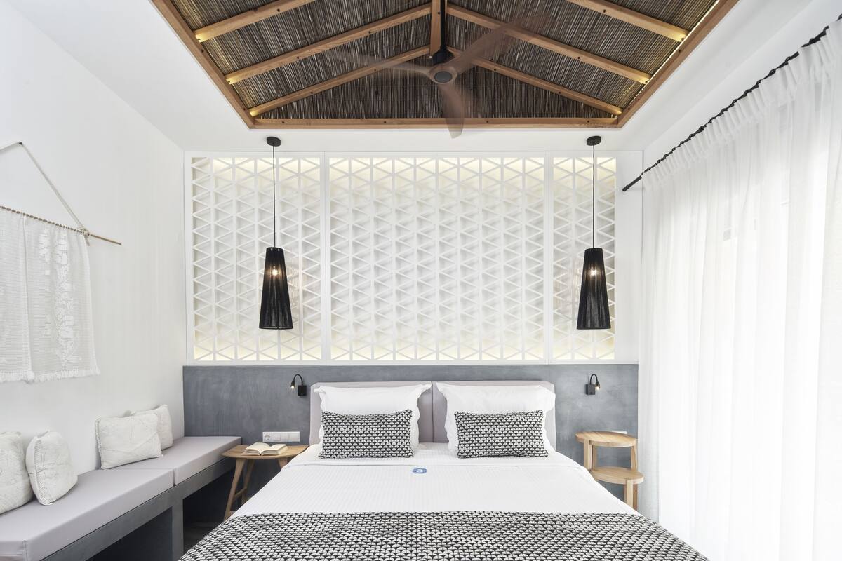 Un dormitorio moderno con cama, asientos tipo banca, lámparas colgantes y ventilador de techo.