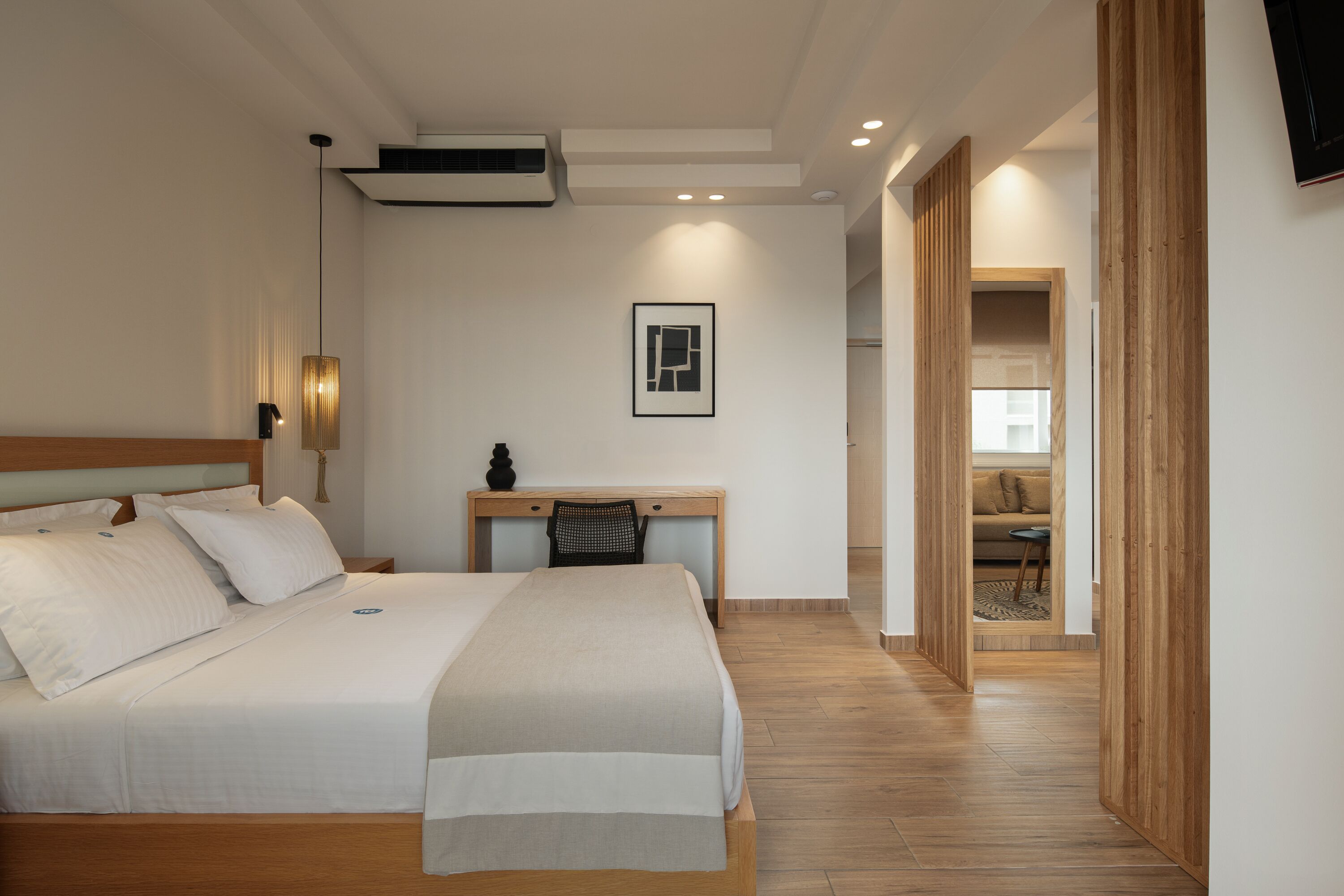A hotel room with a bed, desk, and a view into the living area.
