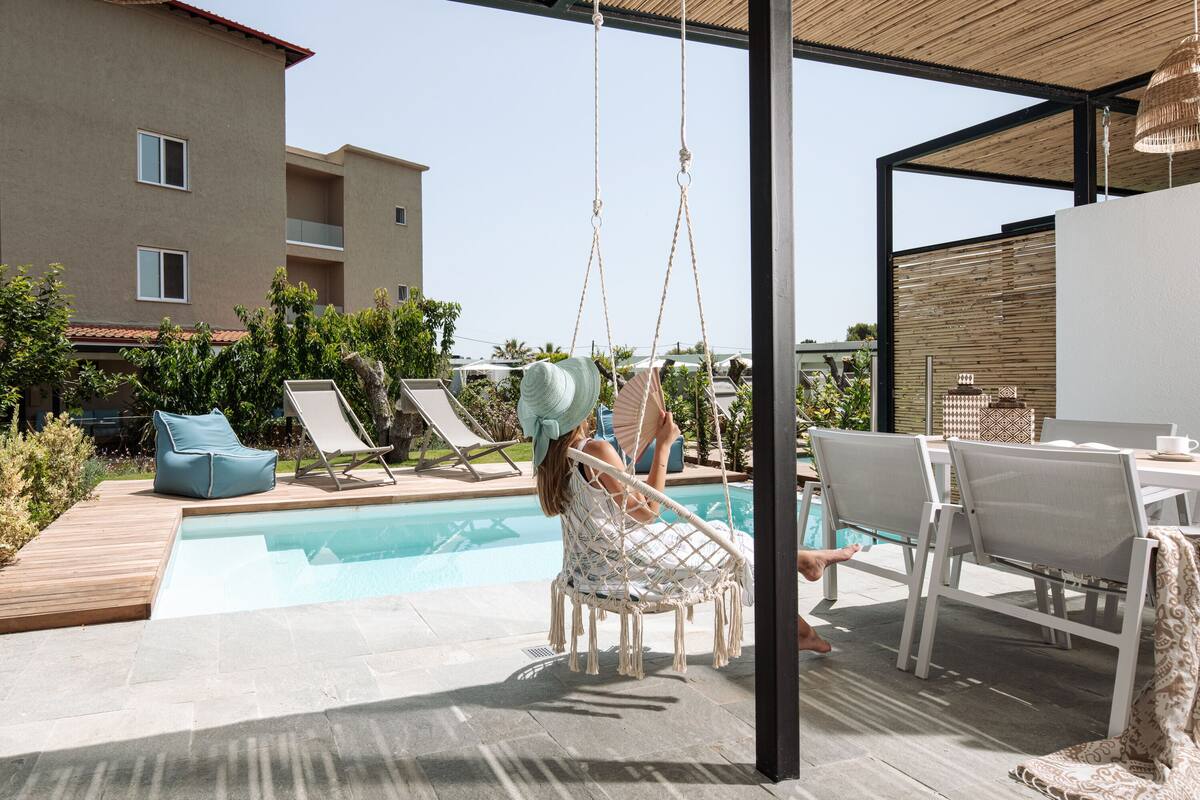 Un área junto a la piscina con una silla colgante, sillones reclinables y una mesa con sillas.
