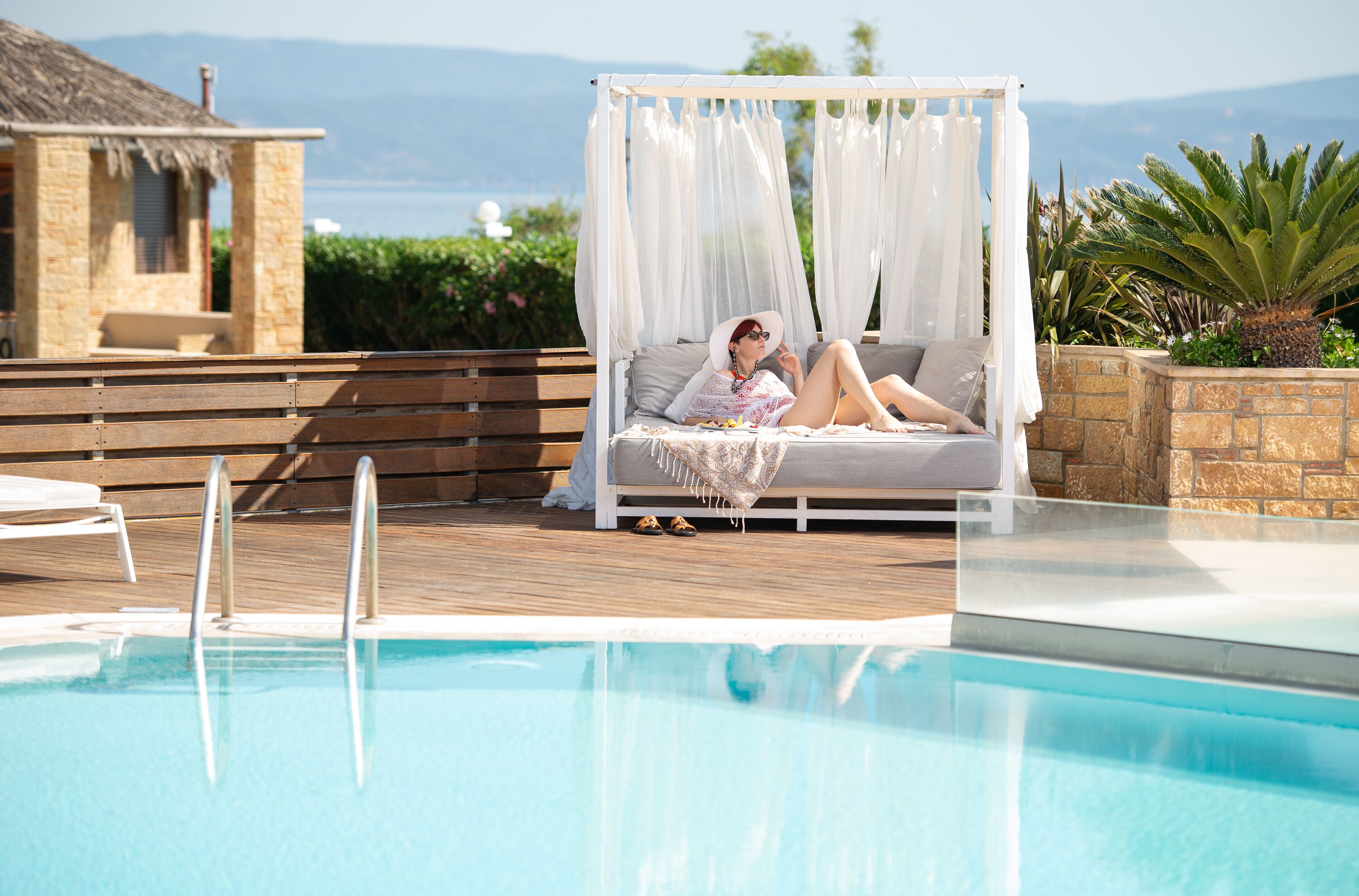A poolside area with a canopy bed, a pool, and a stone building in the background.